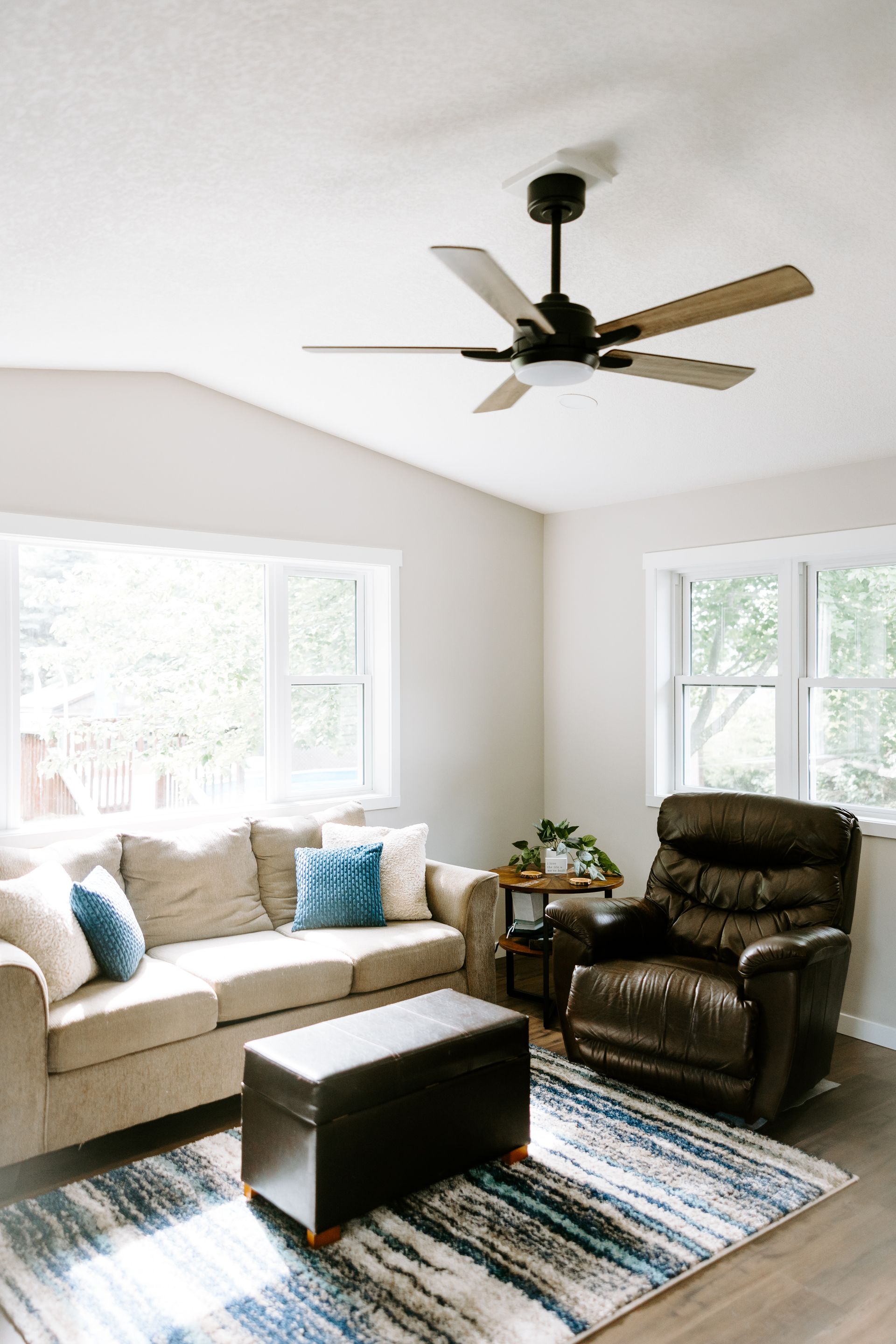 A living room with a couch, chair, coffee table and ceiling fan.