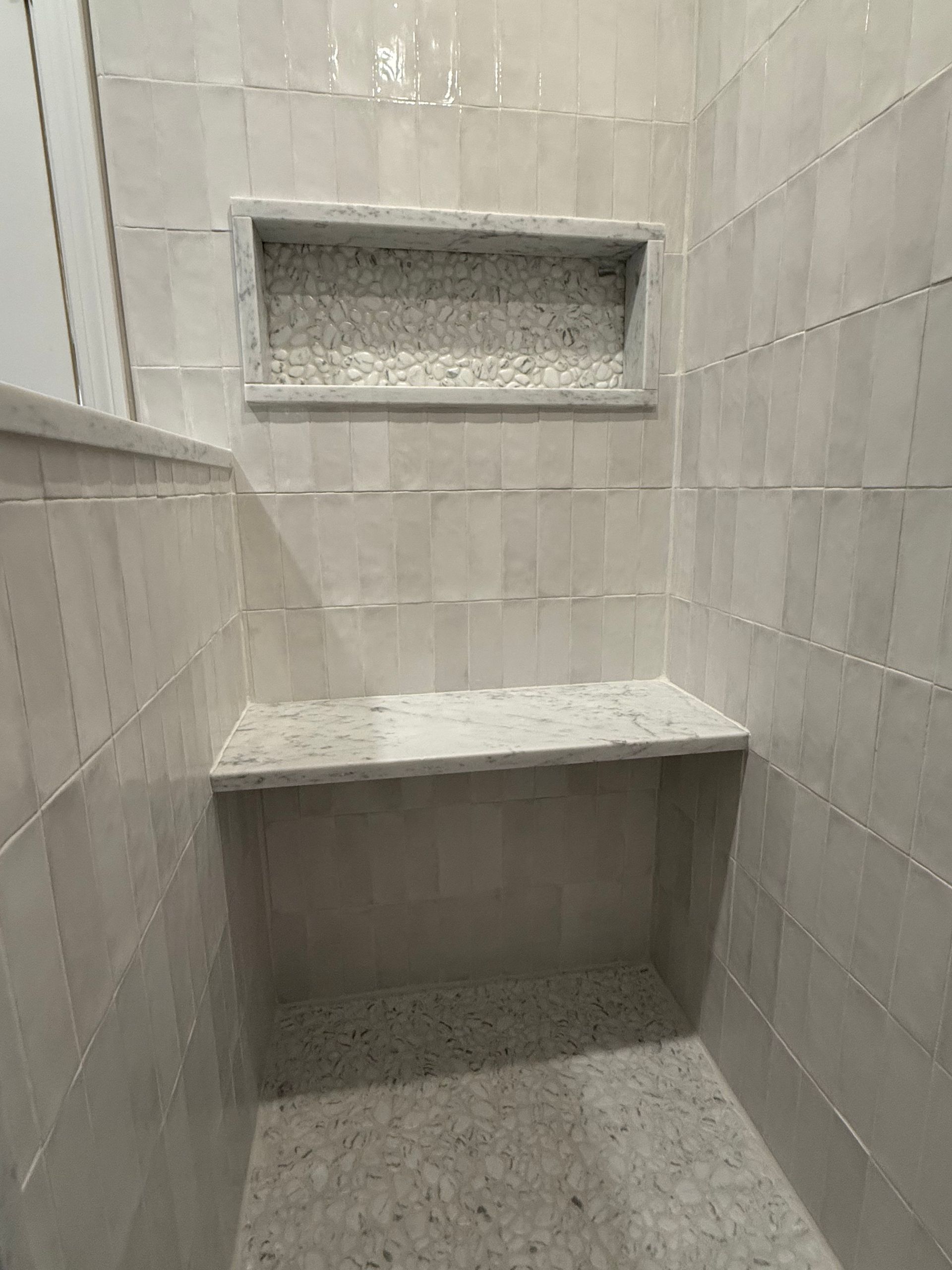 There is a bench in the shower with a shelf above it.