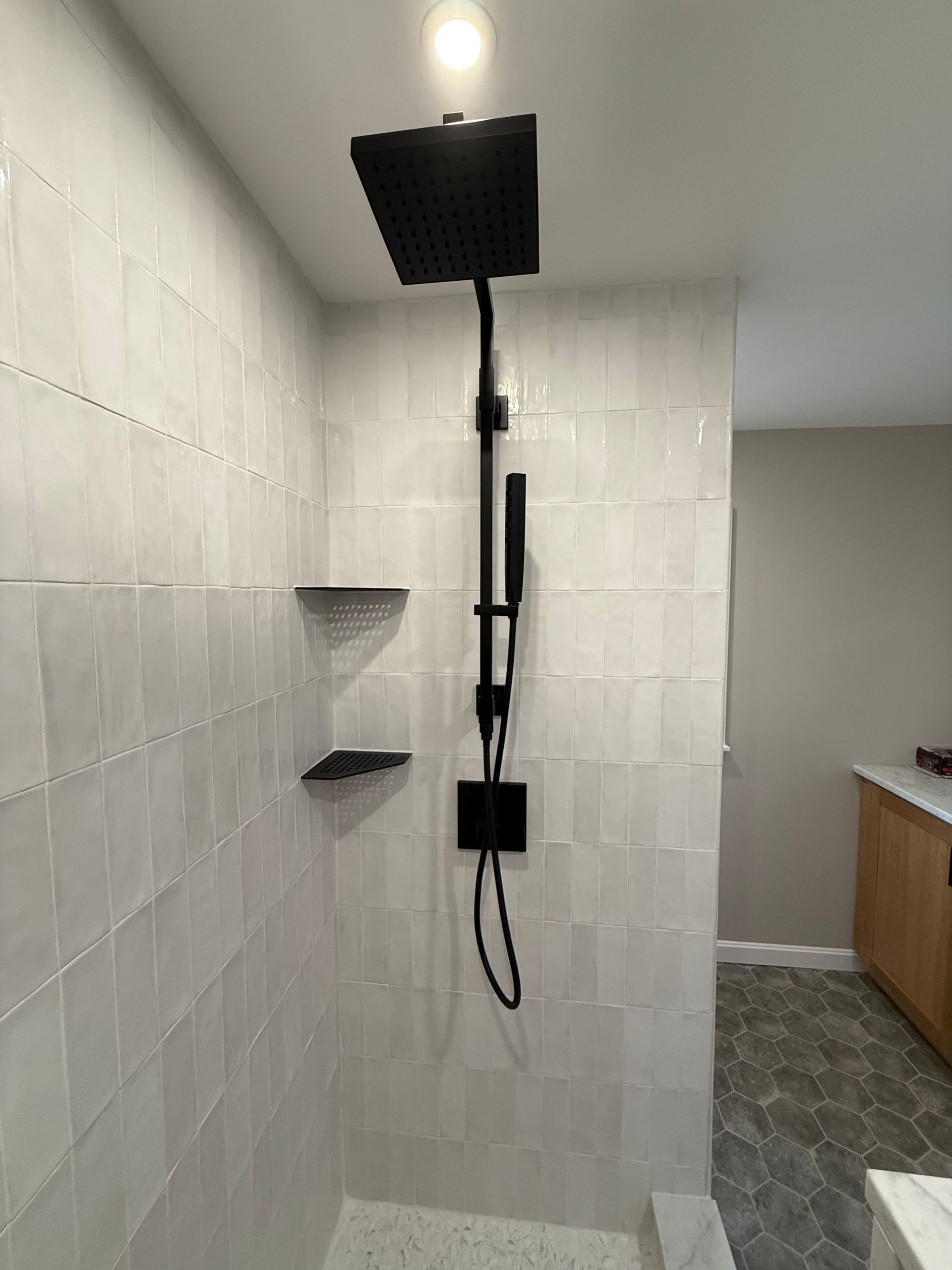 A shower with a black shower head and shelves in a bathroom.