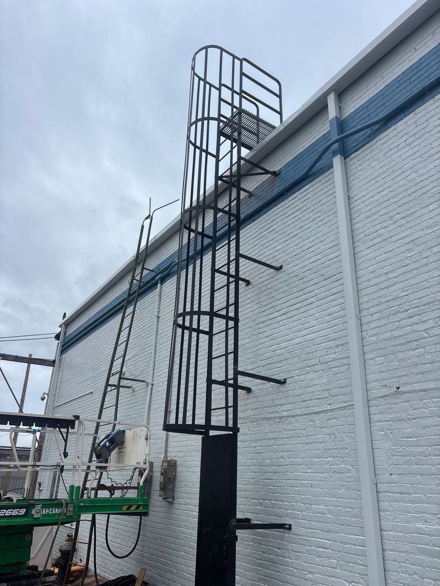 Tall steel rebar cage beside a white brick wall on a construction site under a cloudy sky