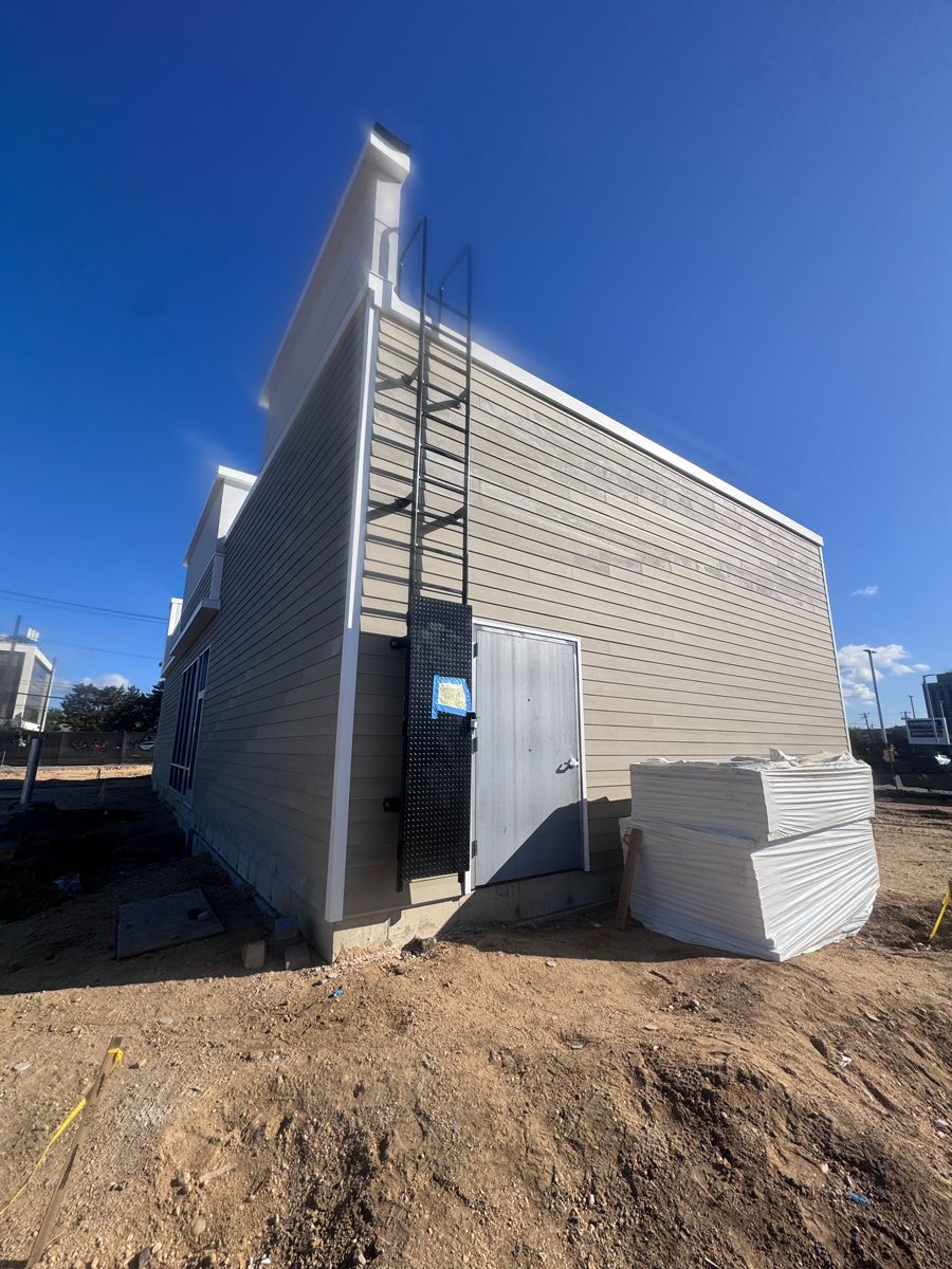 Corrugated metal shed under construction on a dirt lot, with a blue sky overhead