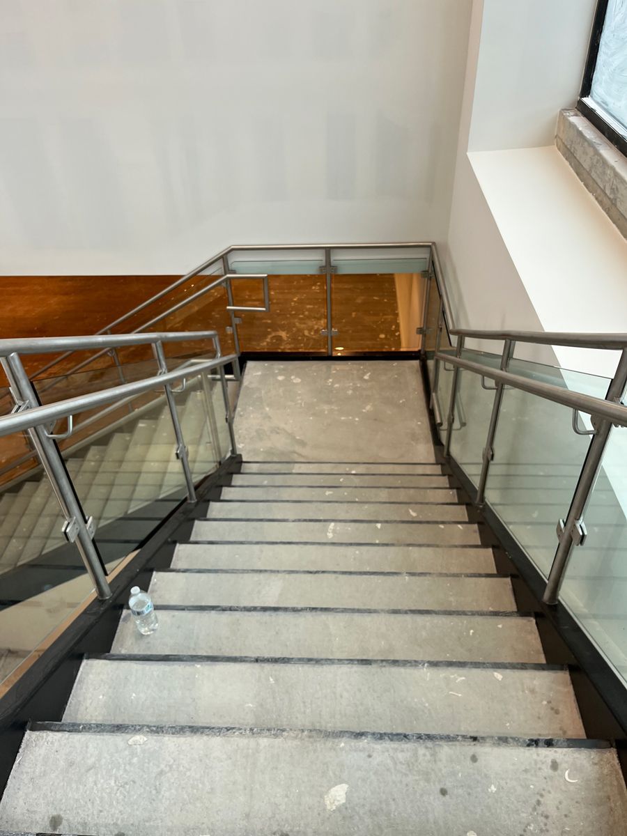 View down a stairwell with gray steps, metal handrails, and a white wall.