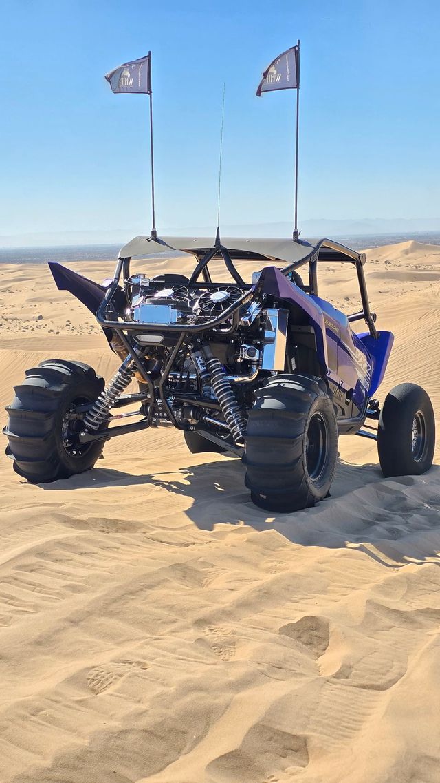 Black off-road dune buggy with flags parked on sandy desert dunes under a clear sky.