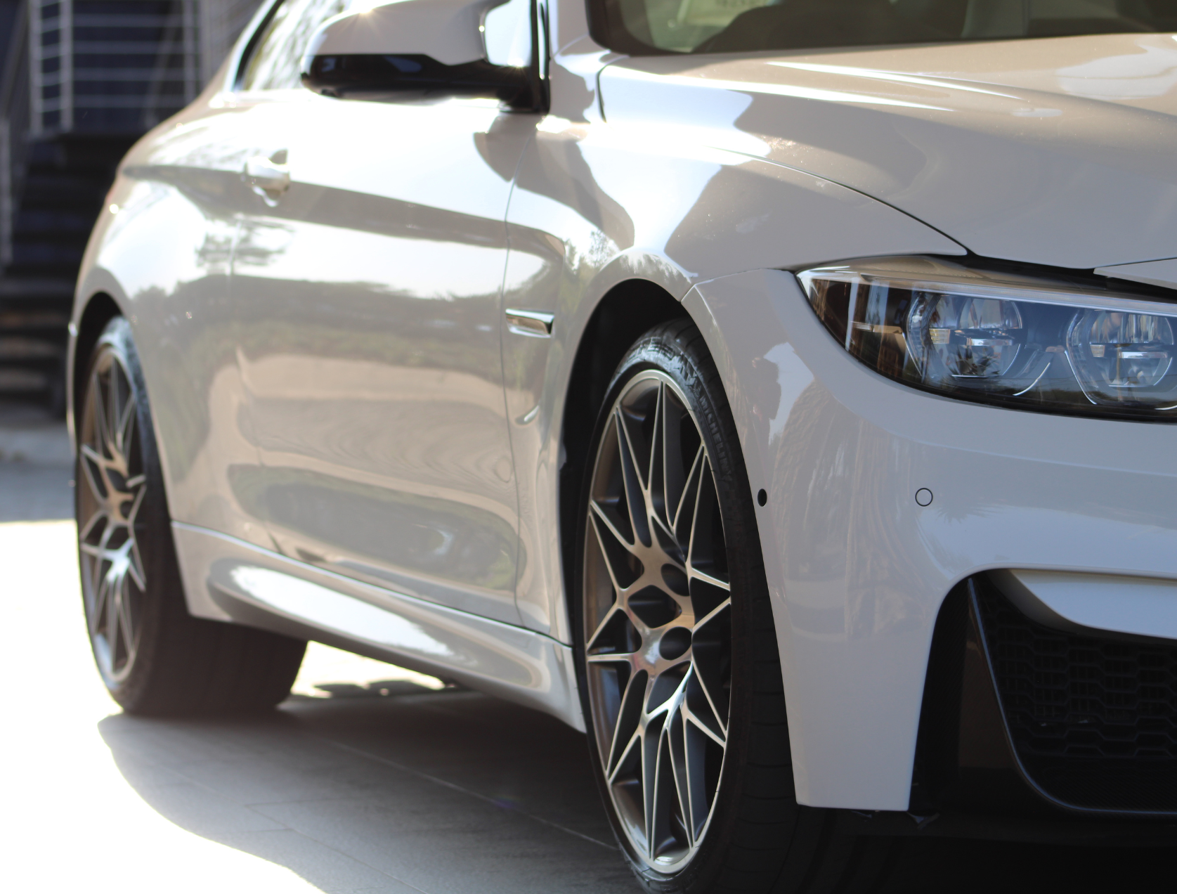 White BMW coupe, close-up of the front, showcasing headlights, wheel, and glossy finish.