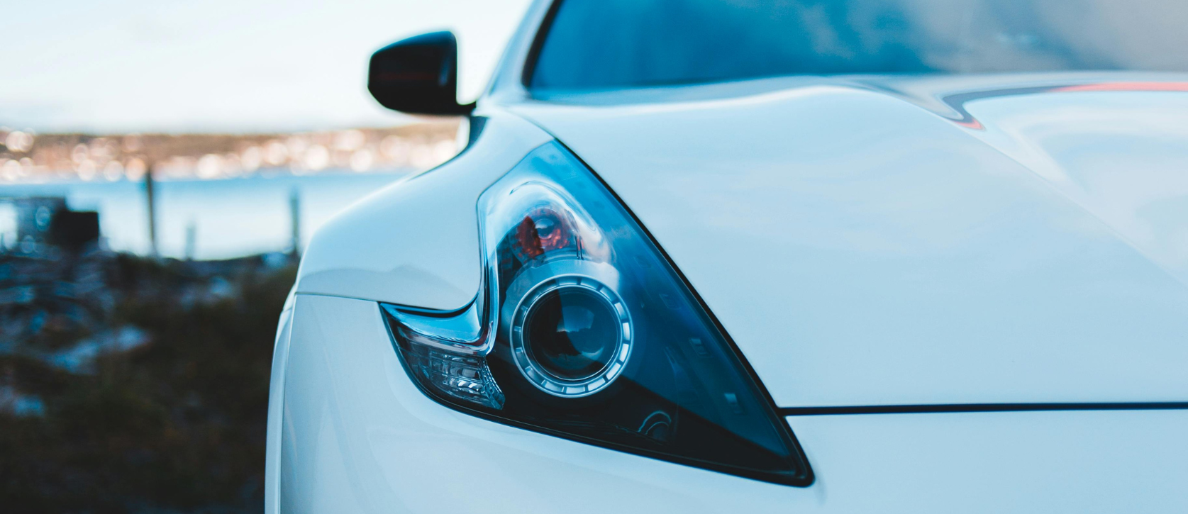 White car headlight close-up, outdoors. Blue-tinted, focused on headlight design.