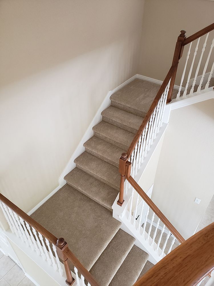 An aerial view of a staircase with carpeted steps and a wooden railing.