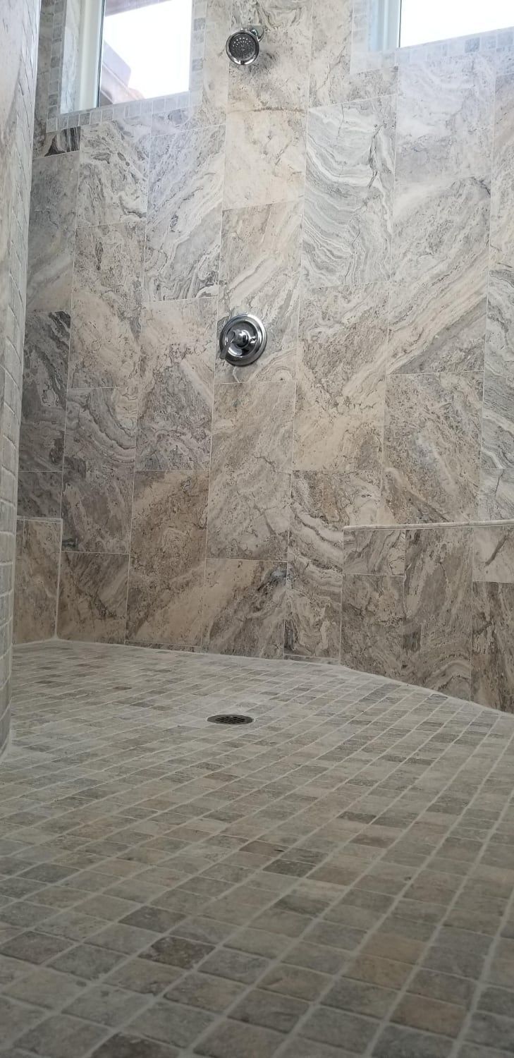 A walk in shower with a tiled floor and marble walls.