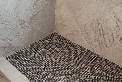 A shower stall with a mosaic tile floor and marble walls.