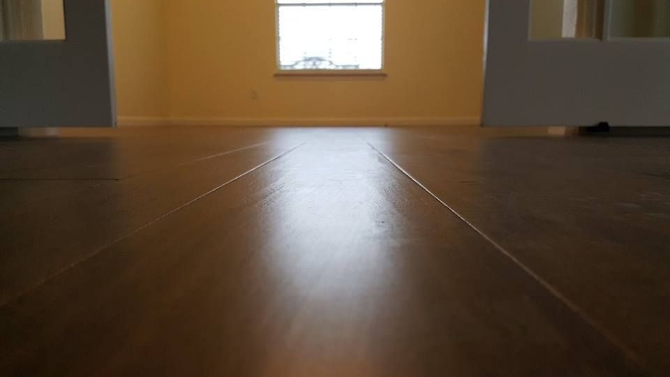 A wooden floor in an empty room with a window in the background.