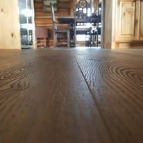 A wooden floor in a kitchen with a table and chairs in the background.