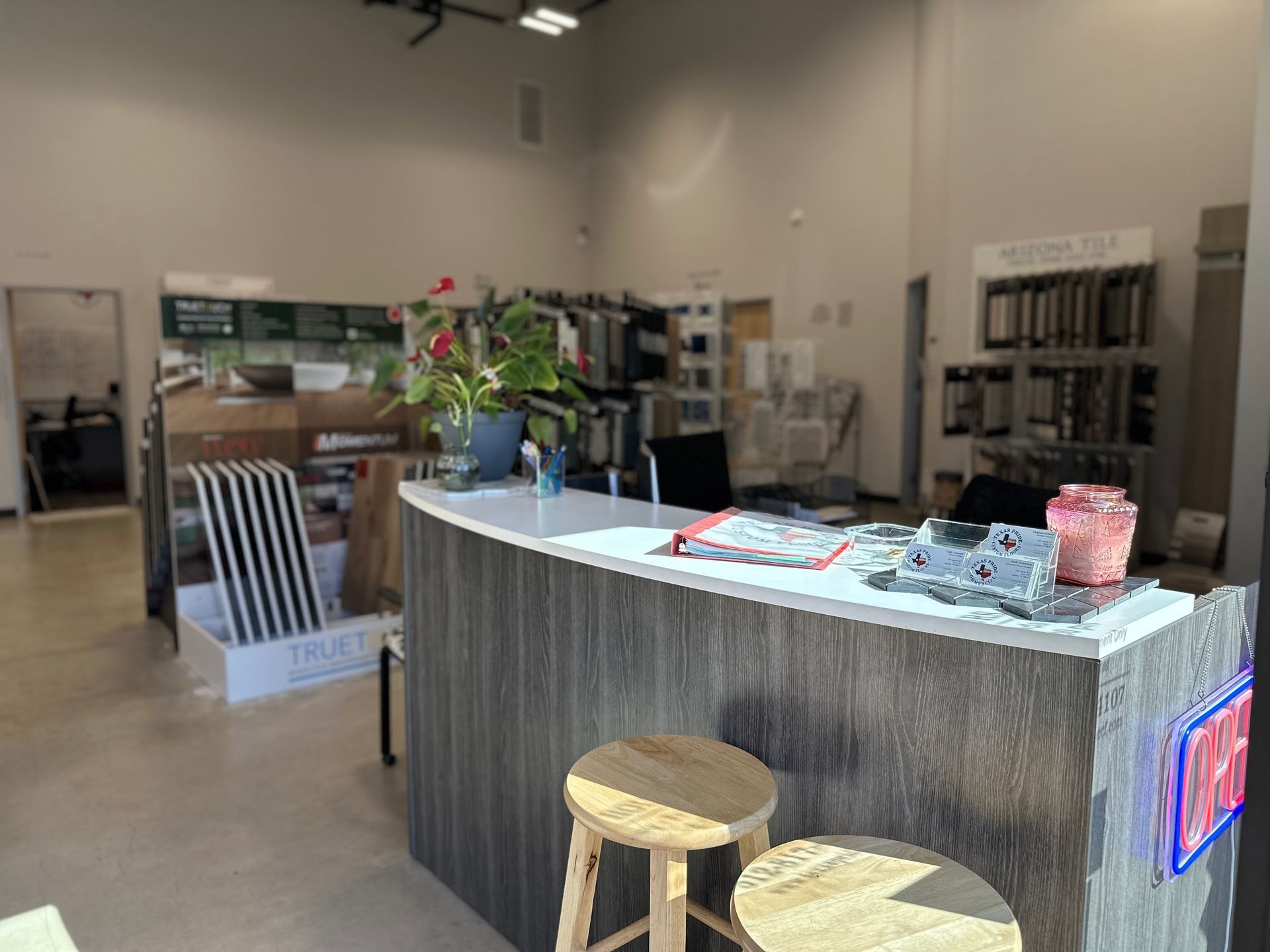 Reception desk in a showroom, wooden stools, samples and displays, natural light.