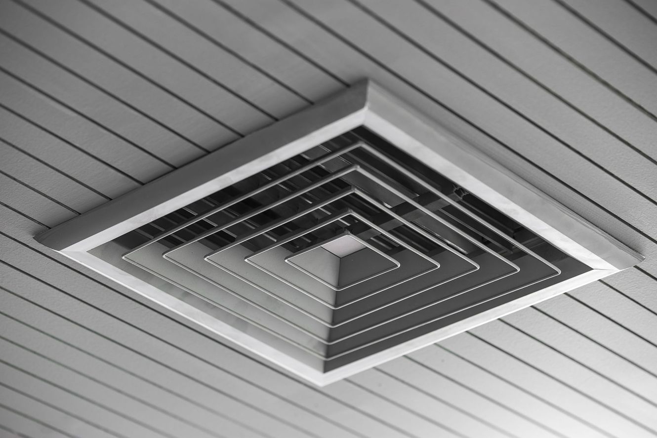 Square, tiered air vent embedded in a white, slatted ceiling.