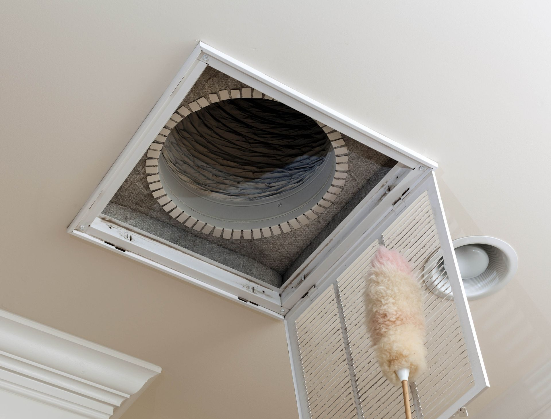 Cleaning a ceiling air vent with a duster; the vent and filter are visible.