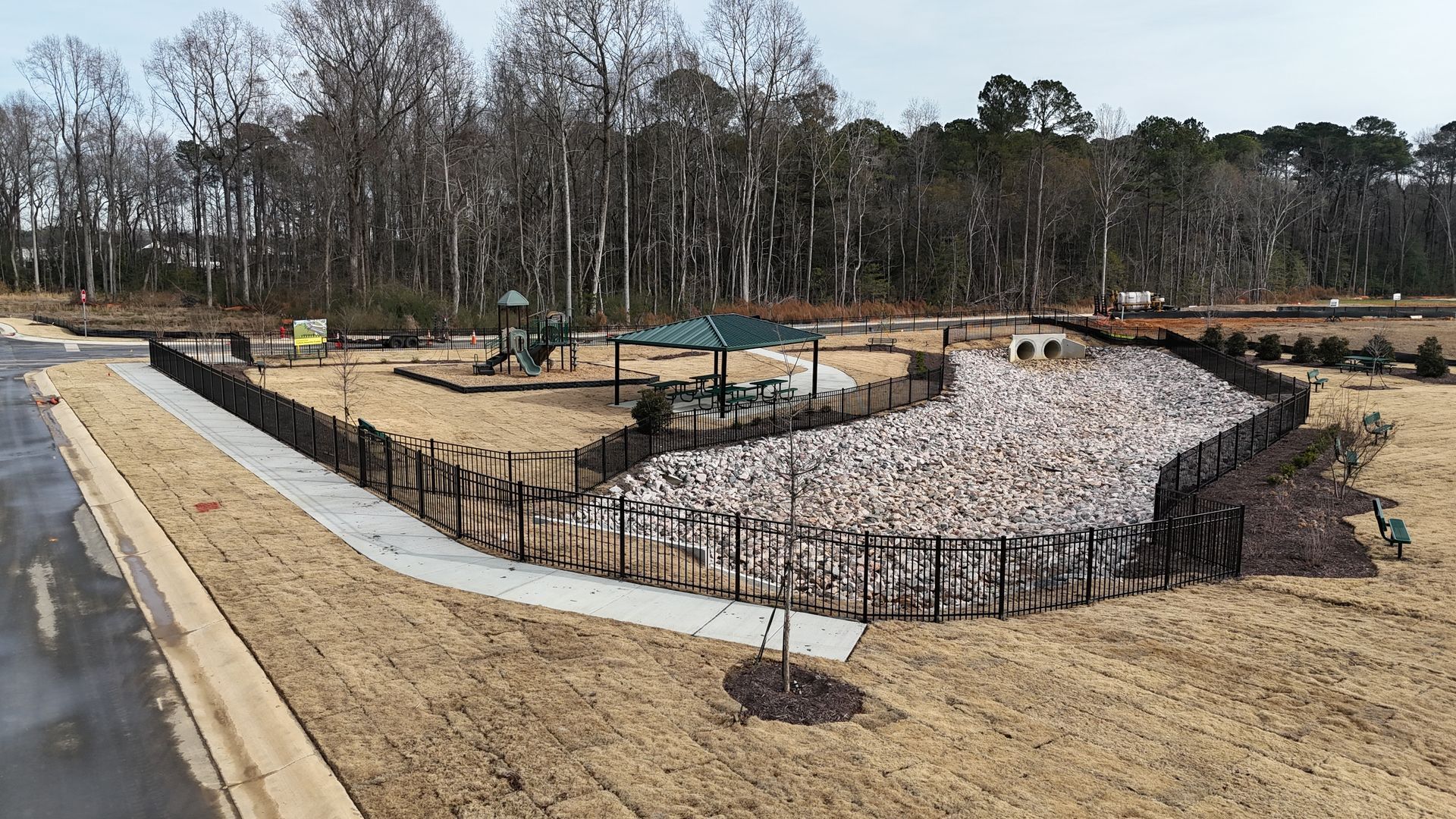 Playground with a stone border and a small shelter surrounded by a fence.