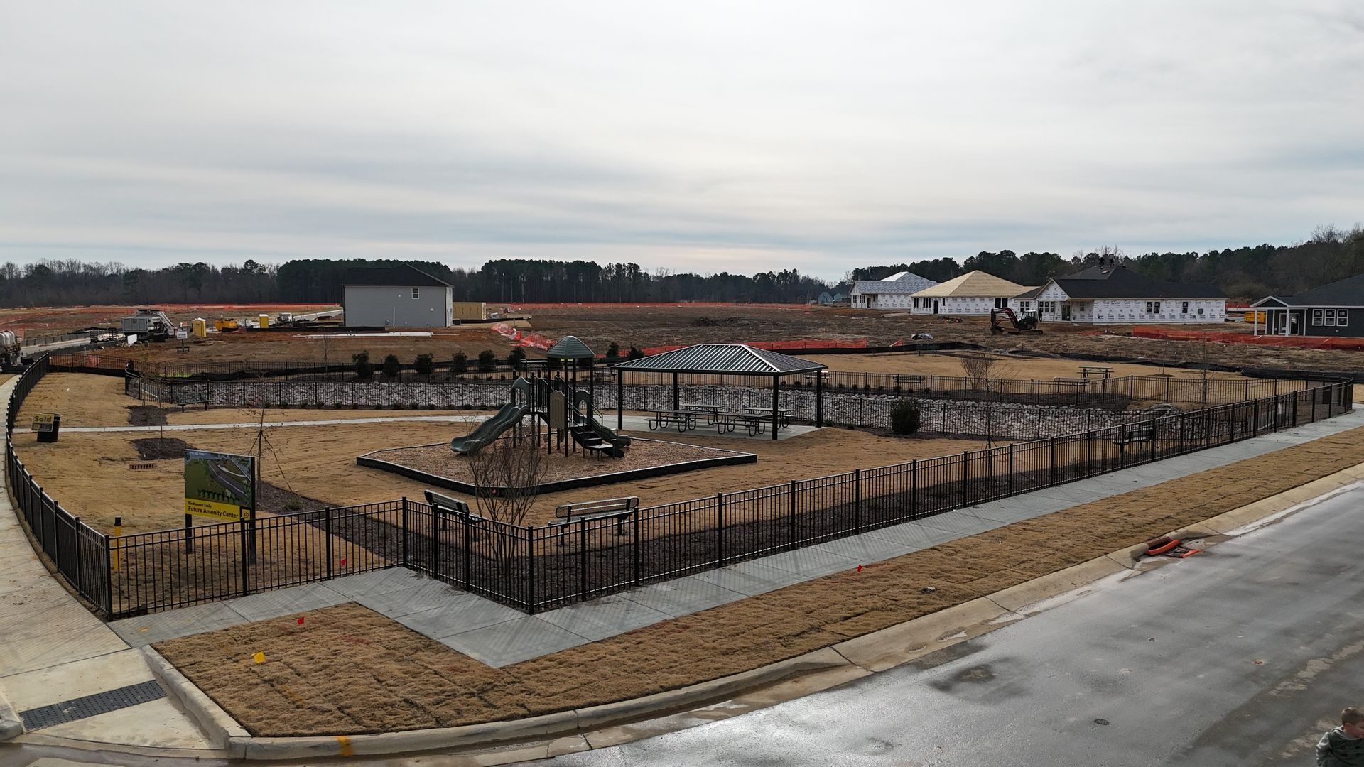 A fenced playground under construction, with visible equipment and surrounding landscape.