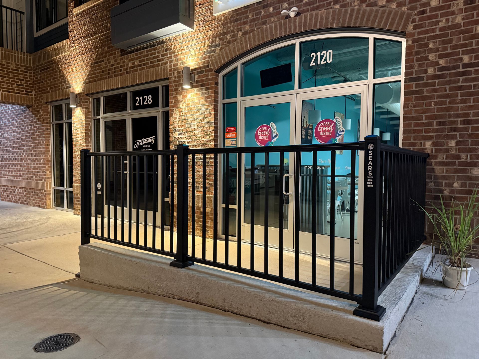 Exterior of a building with brick facade, arched window. Black railing surrounds the entrance. Address is 2120.
