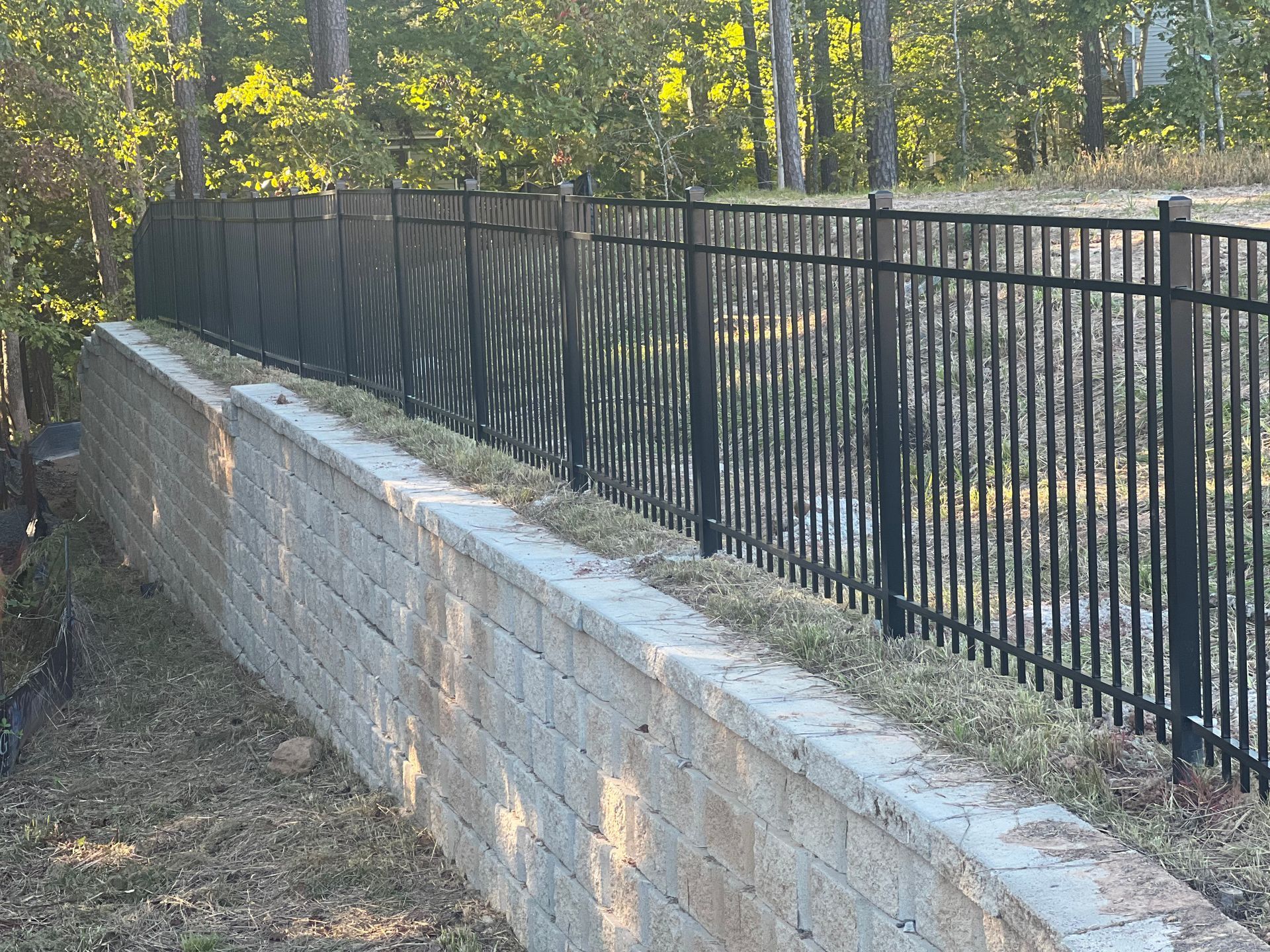 Black metal fence atop a retaining wall, grass growing in between.