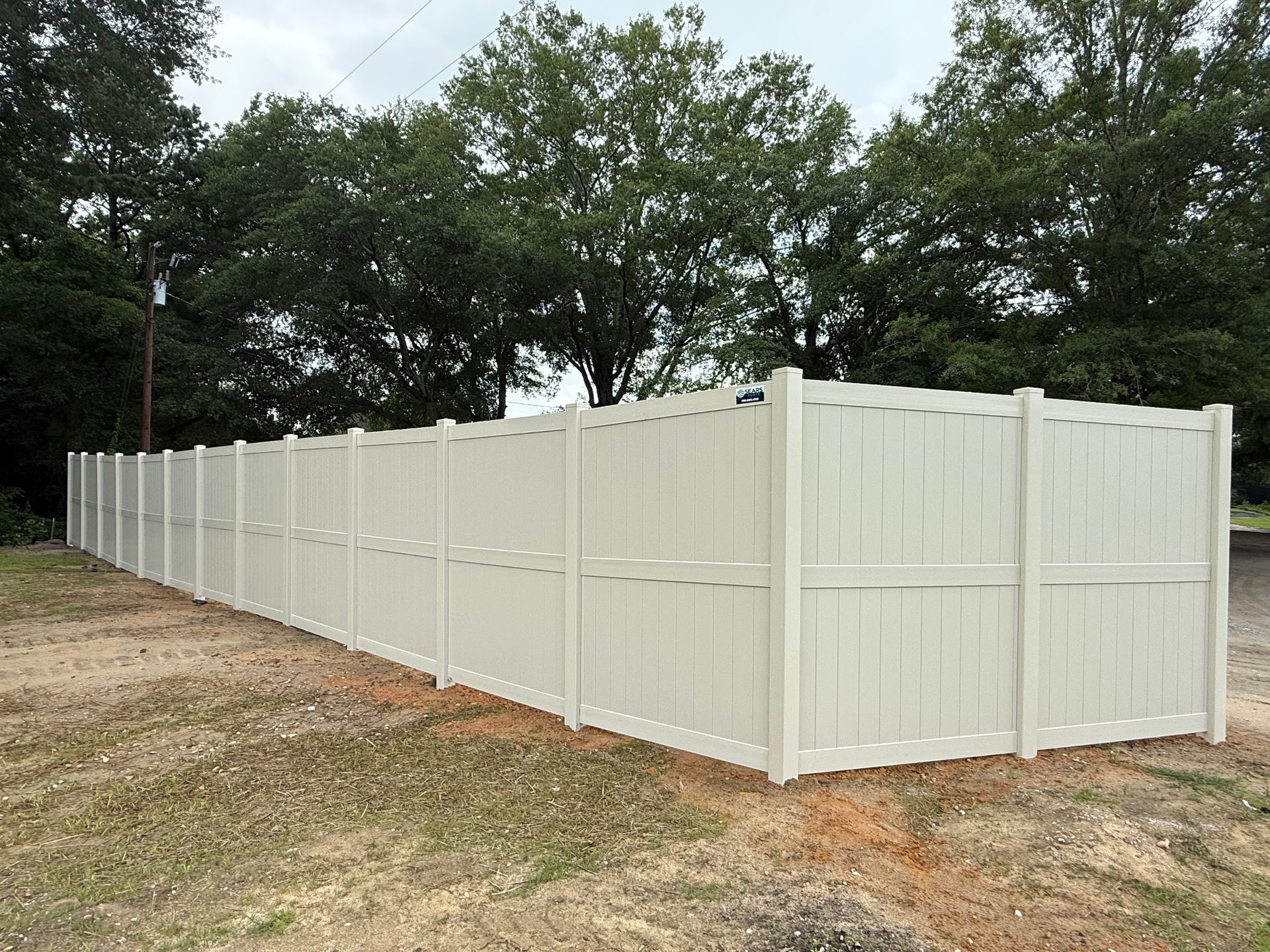 White vinyl privacy fence in a grassy area, with trees in the background.