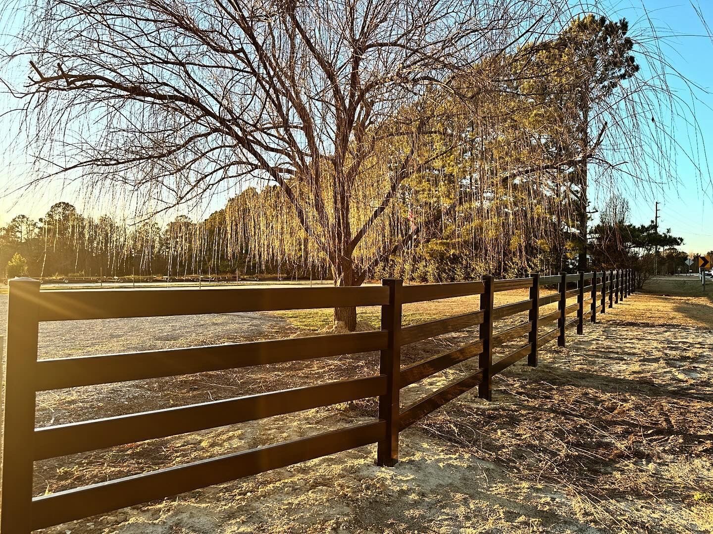 Wooden fence in a rural landscape, with a tree covered in Spanish moss in the background.