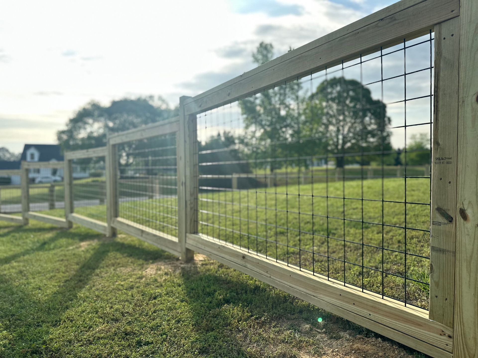 Wooden fence with wire mesh panels, in a grassy field.