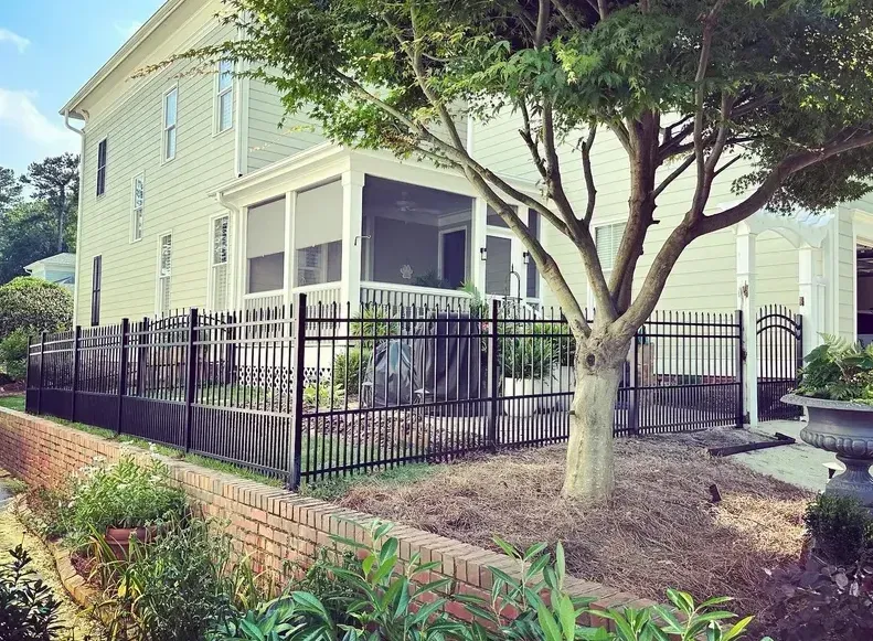 Back view of a light-colored house with a screened porch, black fence, and tree in a yard.