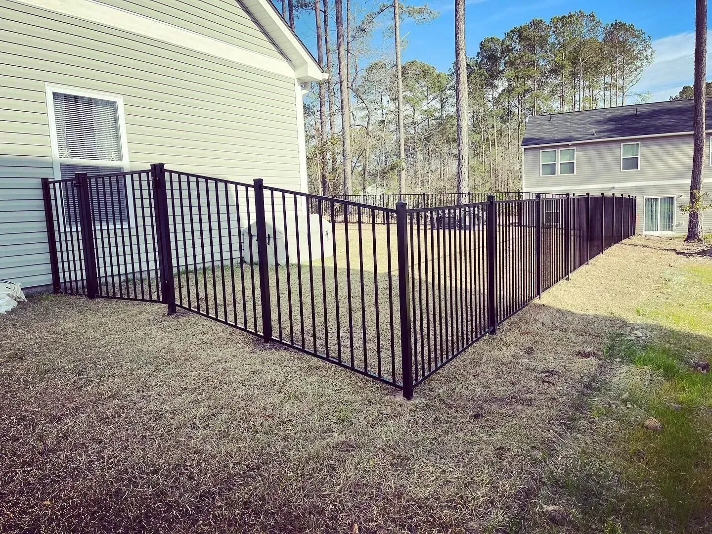 Black metal fence in a yard next to a light green house.