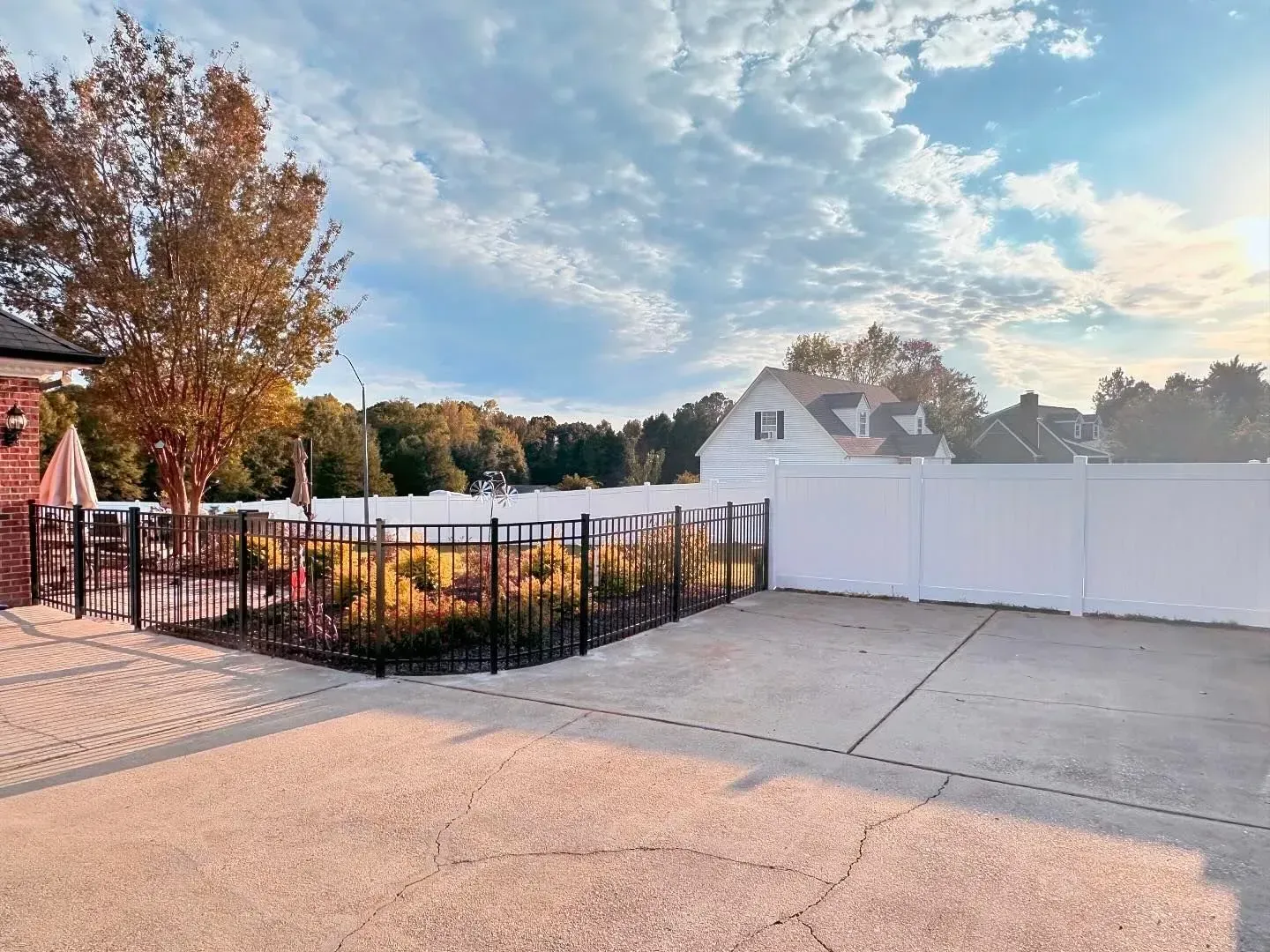 Backyard with a pool, a white fence, and a sunny sky.