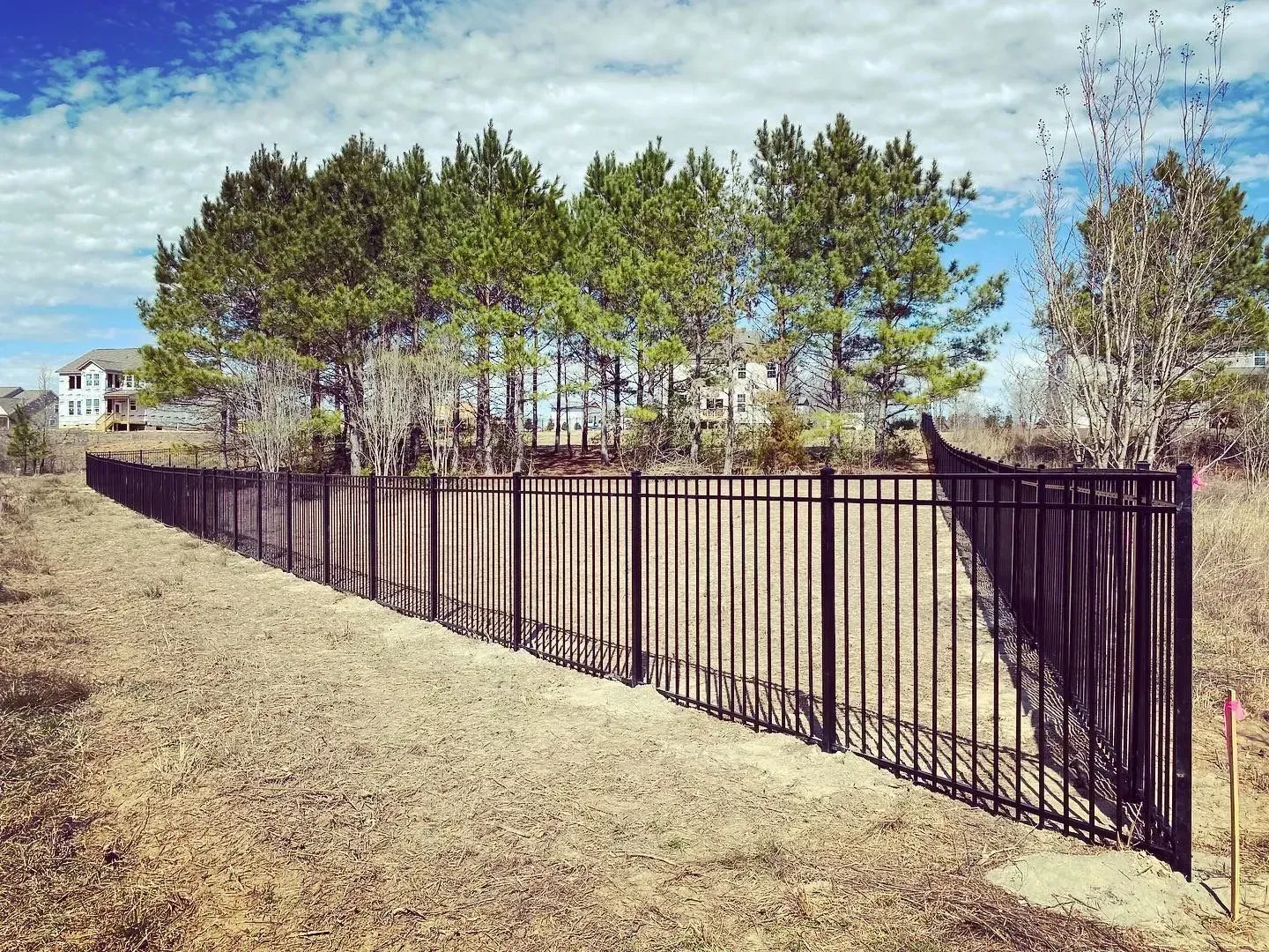 Black metal fence along a dirt area with trees and a blue sky in the background.