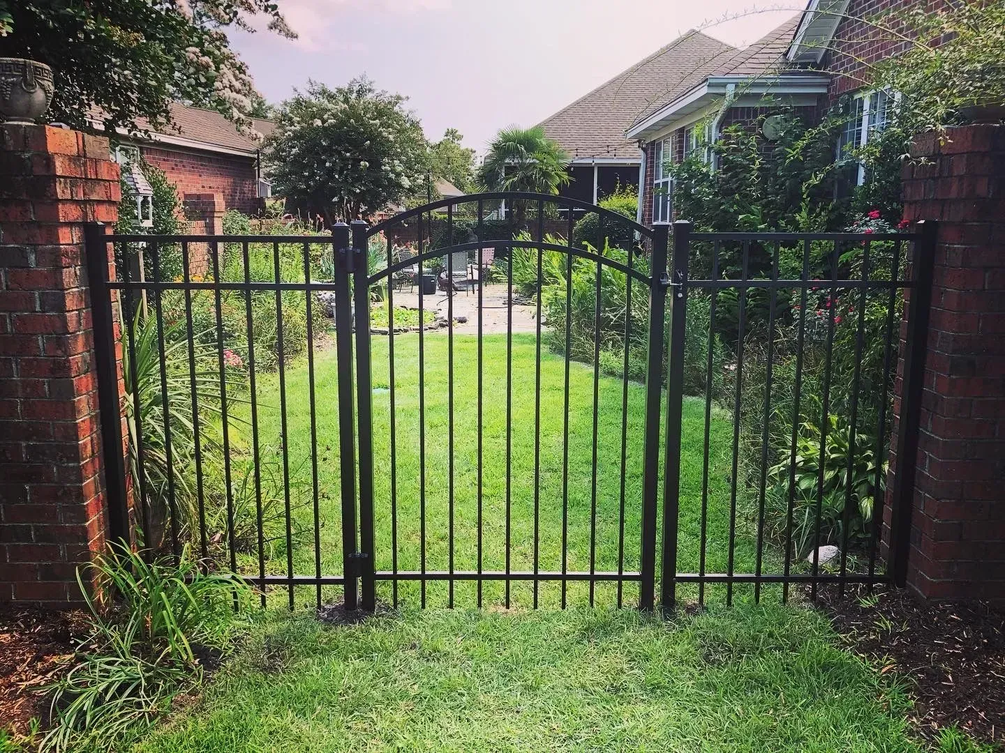 Black metal gate between brick columns, leading to a grassy yard.