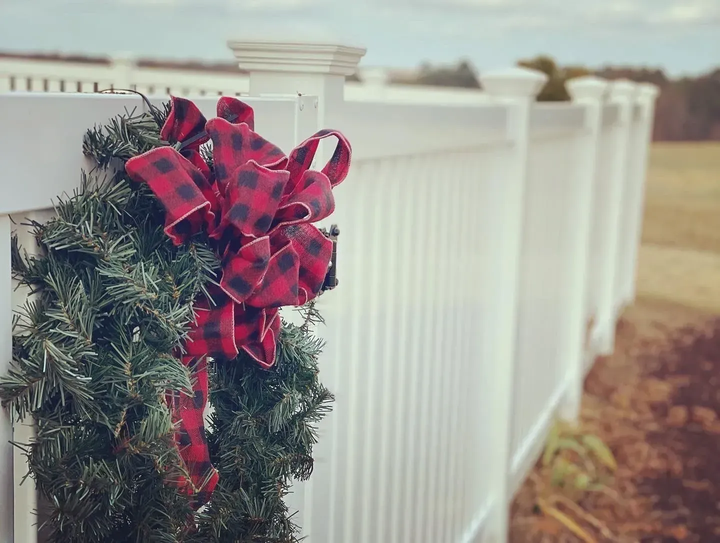 Wreath with red and black buffalo plaid bow on a white fence.