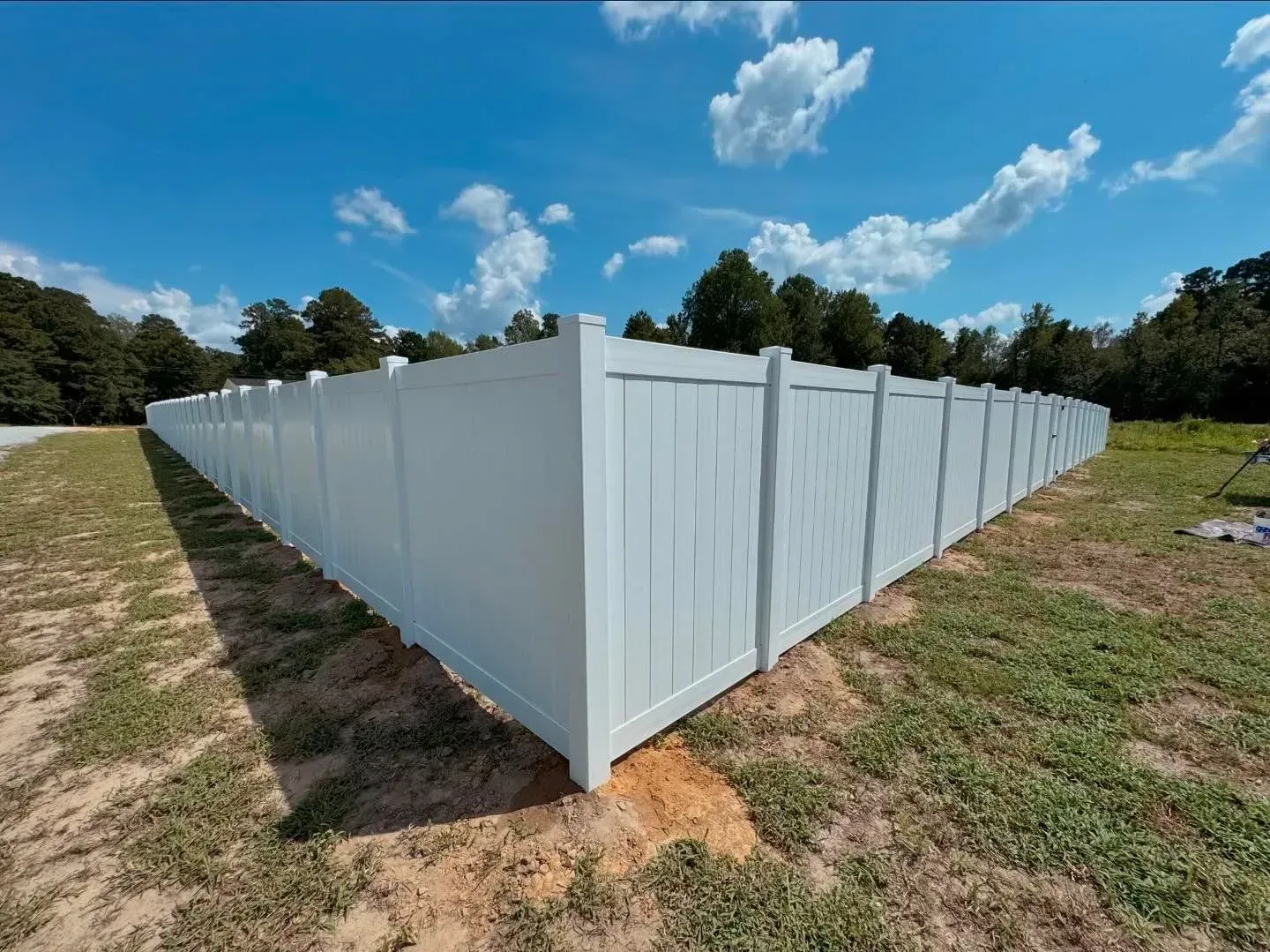 White vinyl fence surrounds a grassy area under a blue sky with clouds.