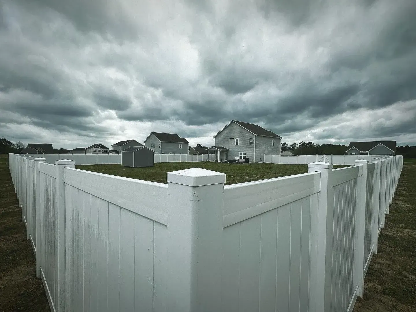 White picket fence surrounds several houses under a cloudy sky.