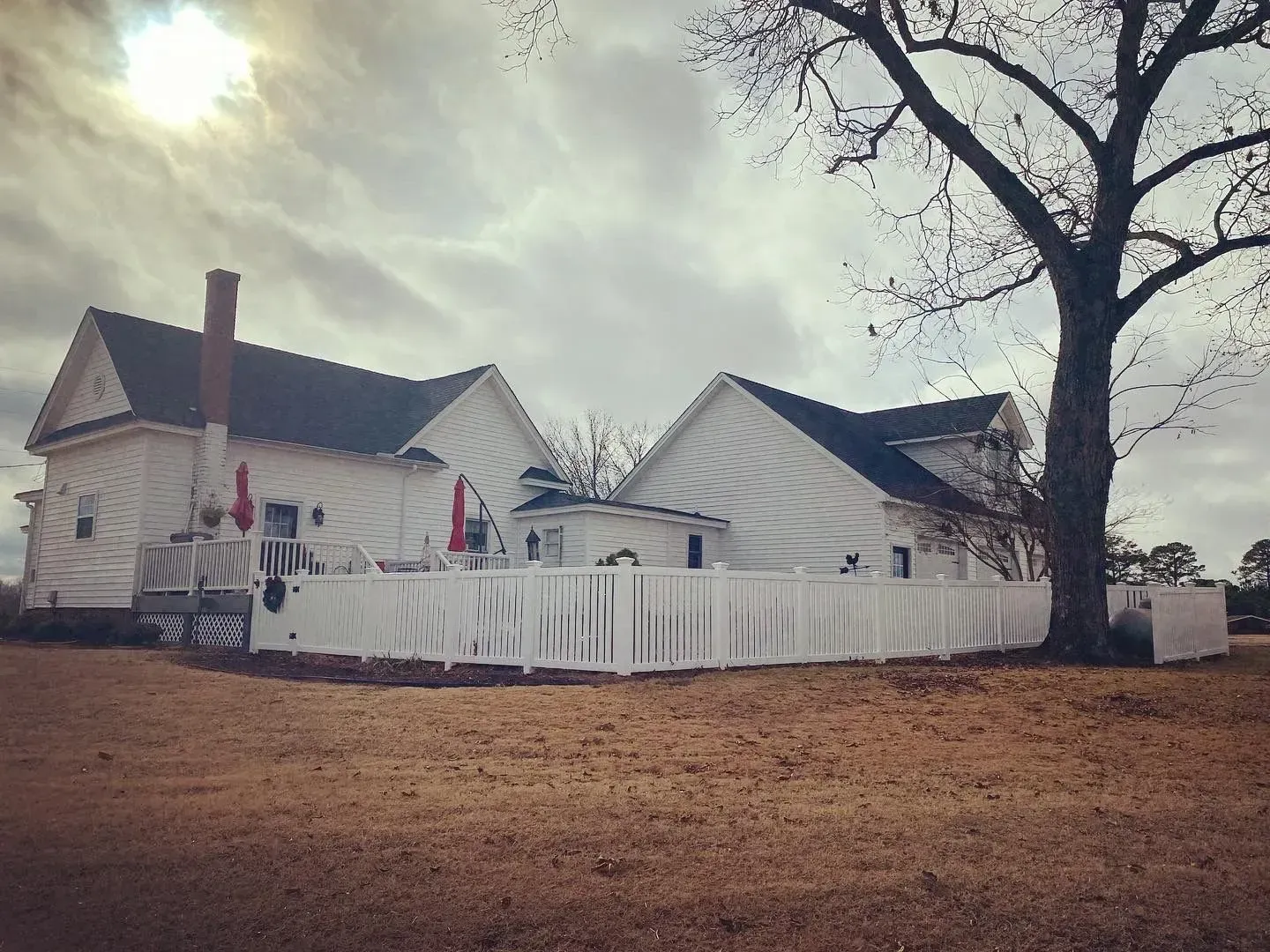White house with fence, tree, and cloudy sky.