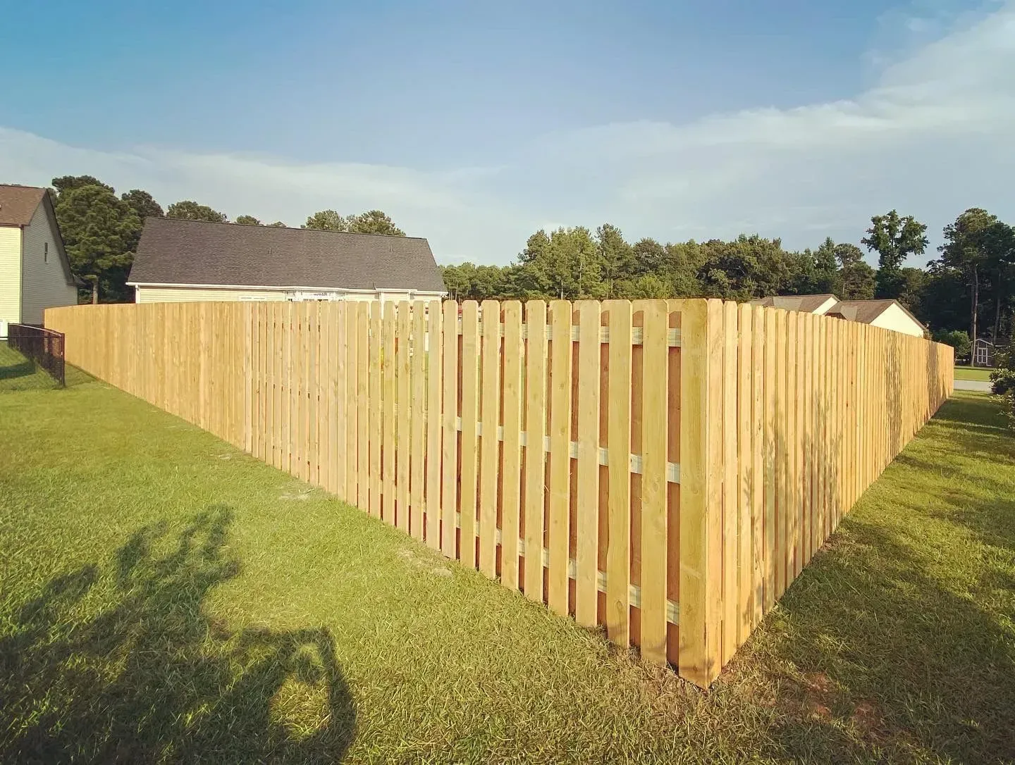 Wooden fence enclosing a grassy yard on a sunny day.