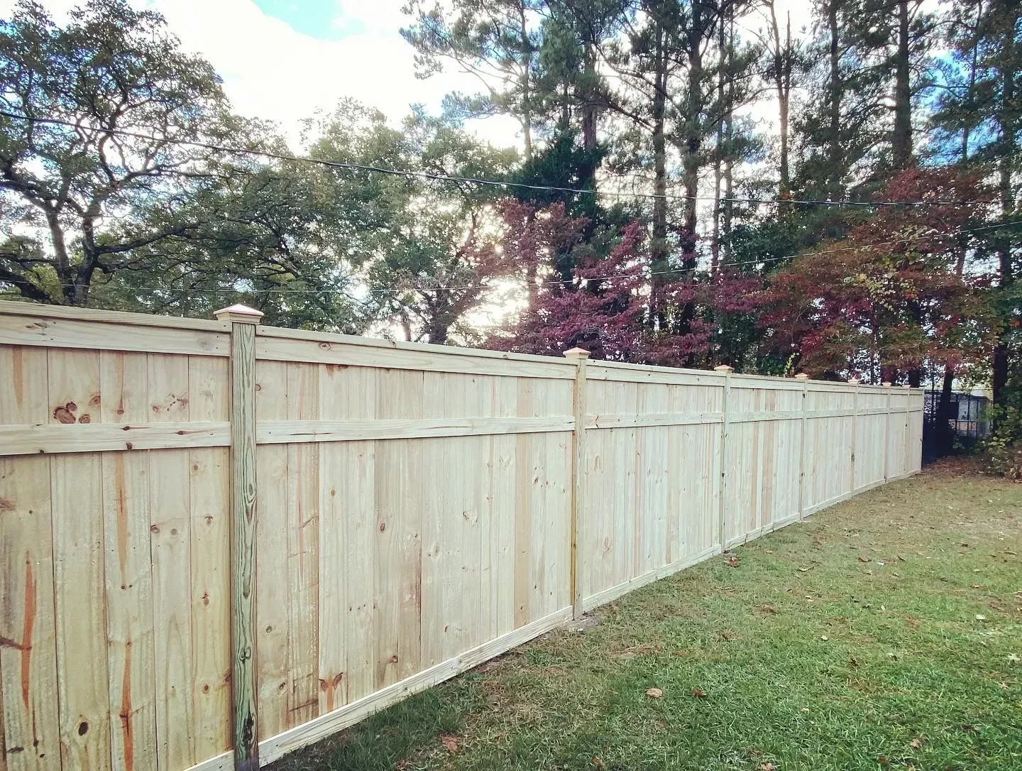 Wooden fence in a yard with trees in the background and a green lawn in the foreground.