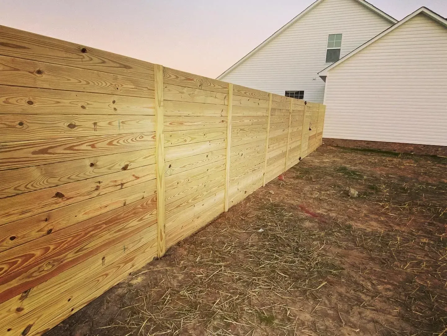 Wooden fence in front of two white houses. The fence is made of horizontal planks.