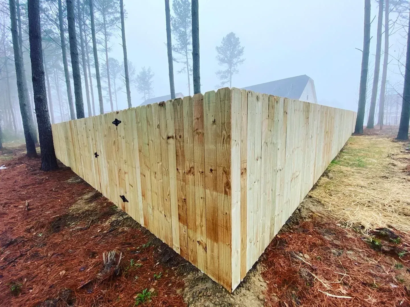 Wooden fence in the shape of a triangle corner in a wooded area with tall trees and a misty background.
