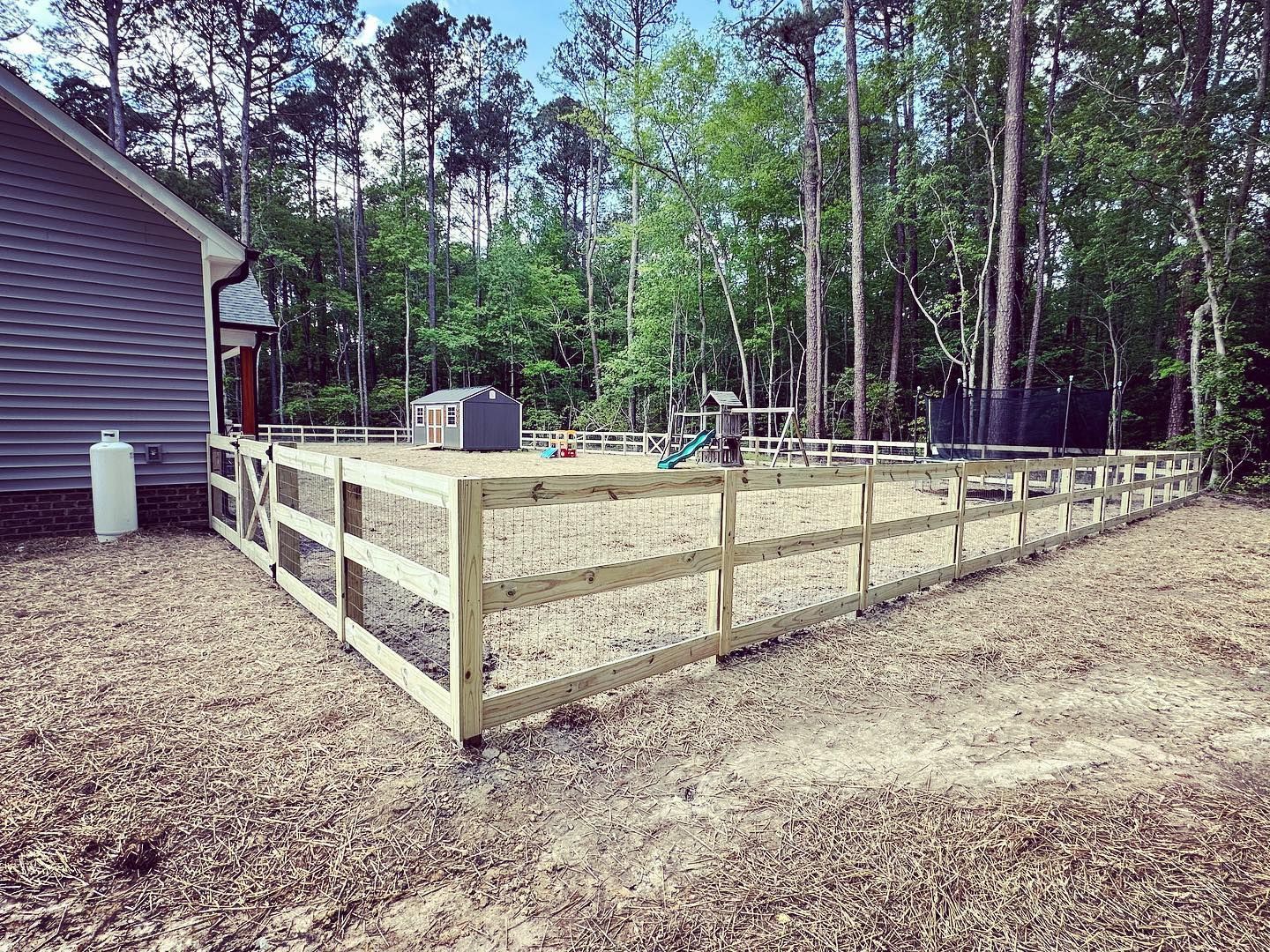 Wooden fence surrounding a gravel yard next to a house and trees.