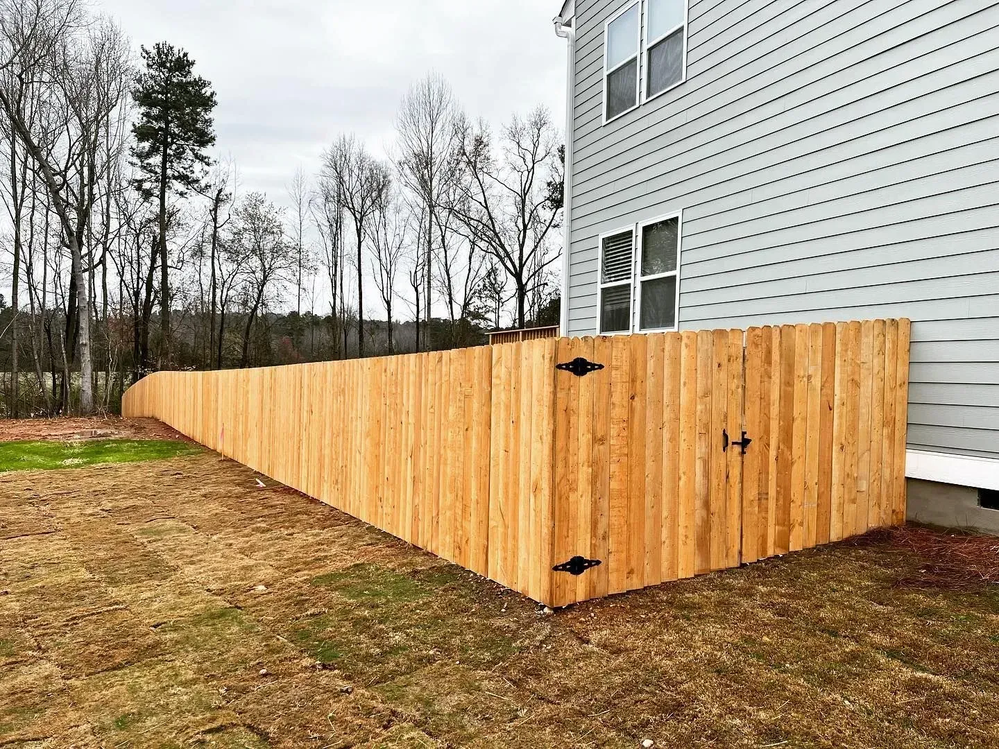 Wooden fence surrounding a house, with a gate, on a grassy lawn.