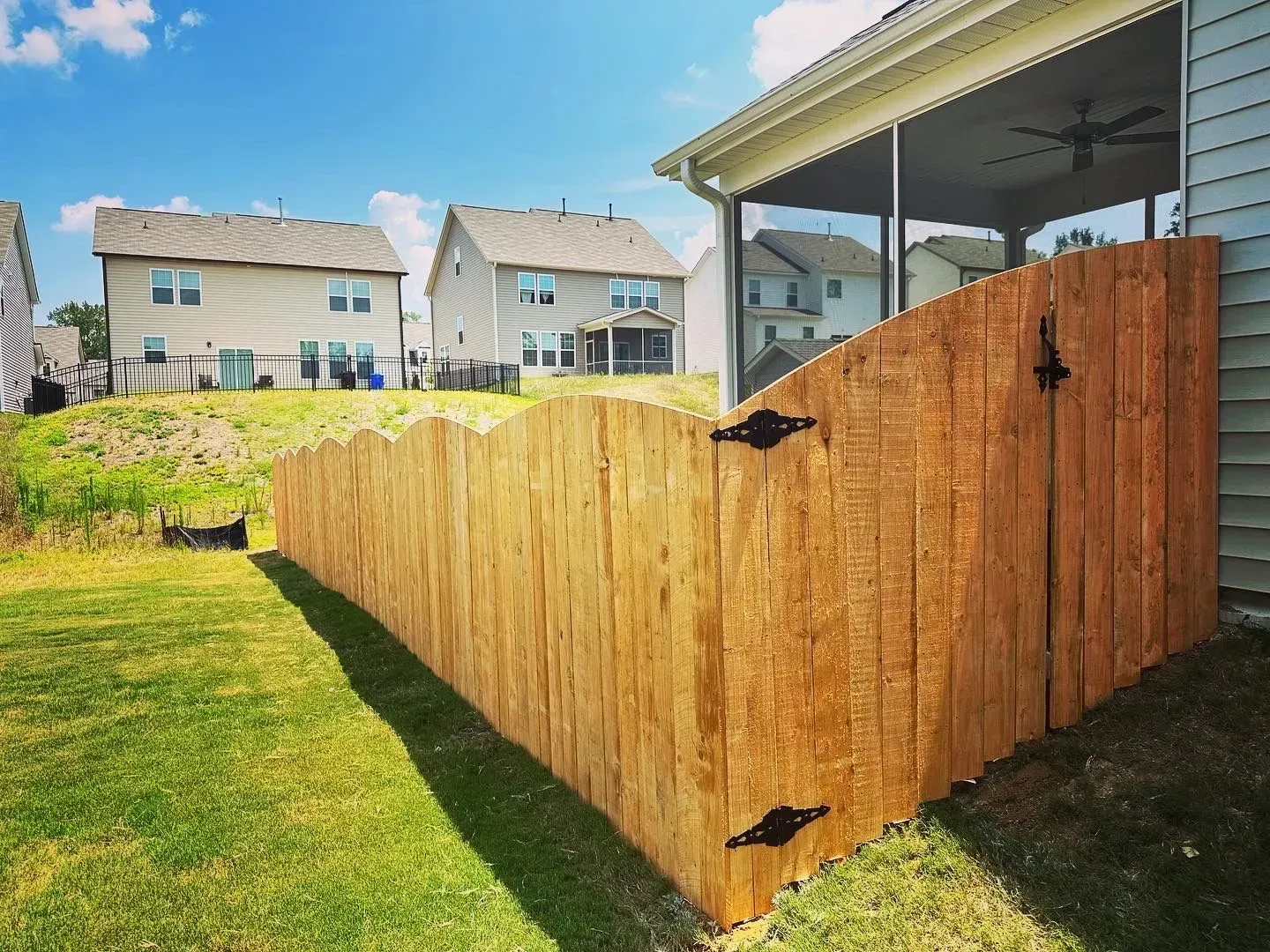 Wooden fence curving around a backyard, beside a house with a screened-in porch. Sunny day.