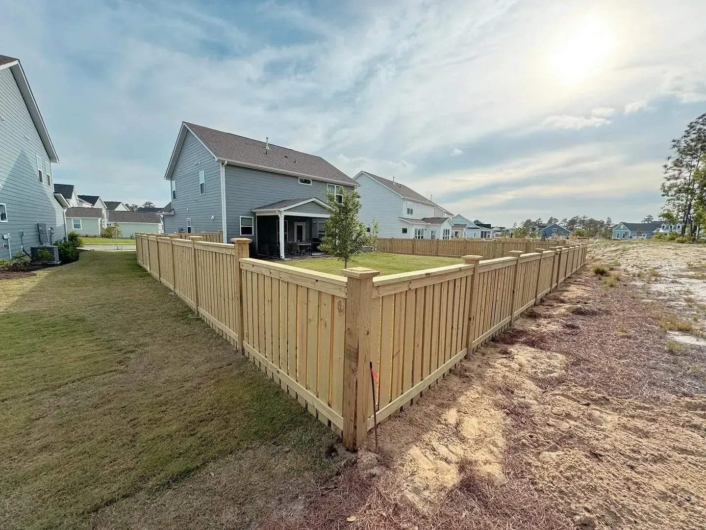 Wooden fence surrounds a house with a gray exterior on a sunny day.