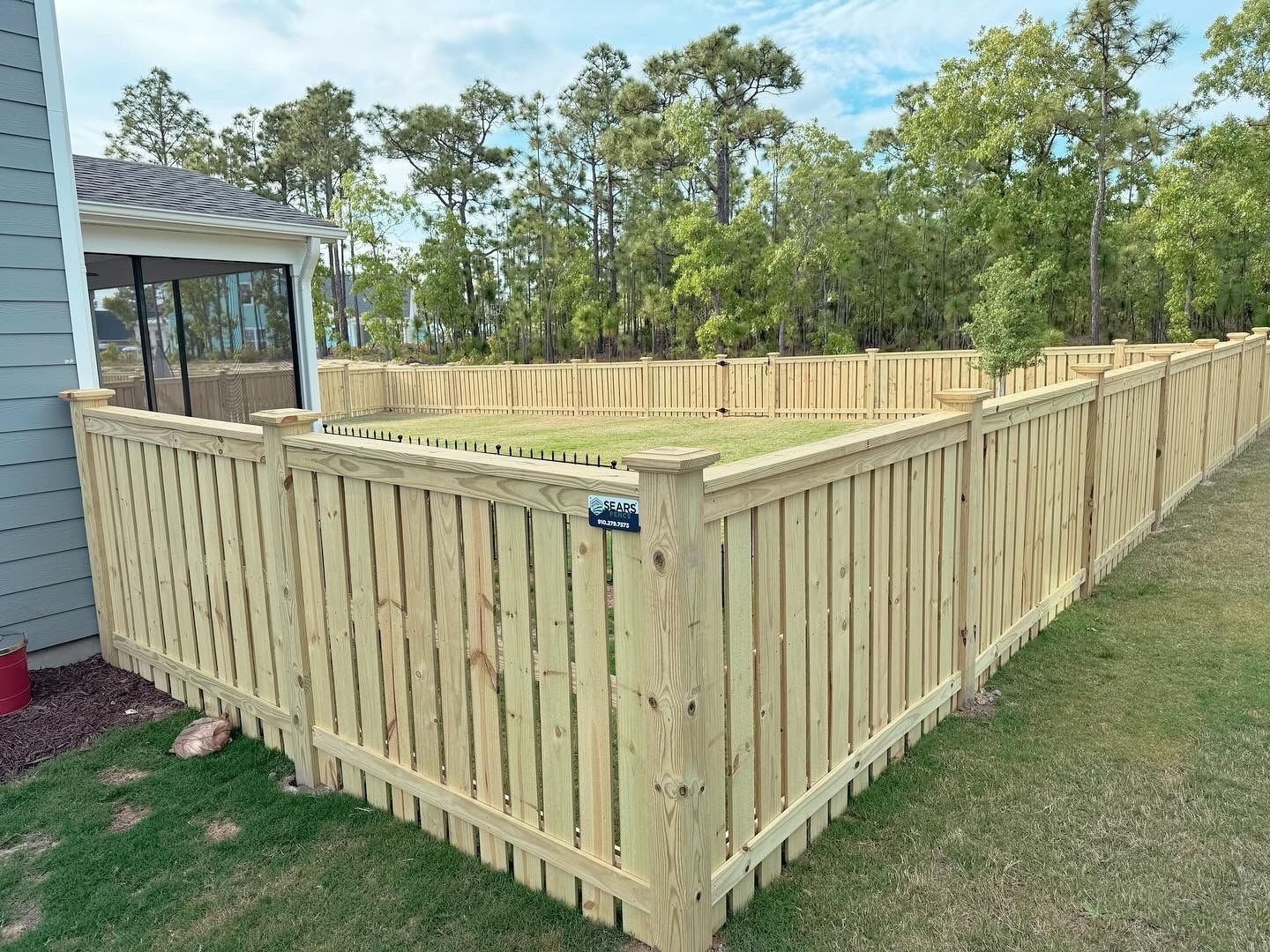 Wooden fence surrounding a grassy yard, trees in the background, a house visible to the left.