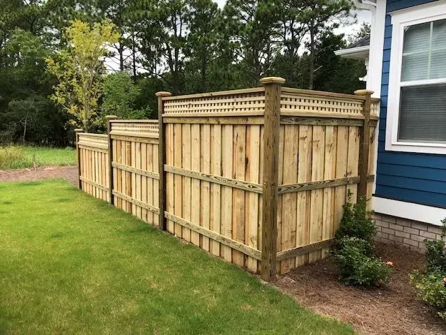 Wooden fence enclosing a grassy area beside a blue house; trees in the background.
