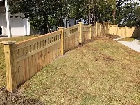 Wooden fence on a slight hill, with grass in front and trees in the background, daytime.