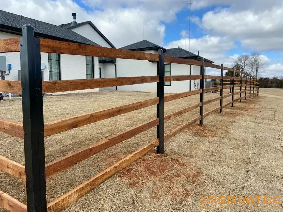 Wooden fence with black posts in front of a white house with a dark roof.