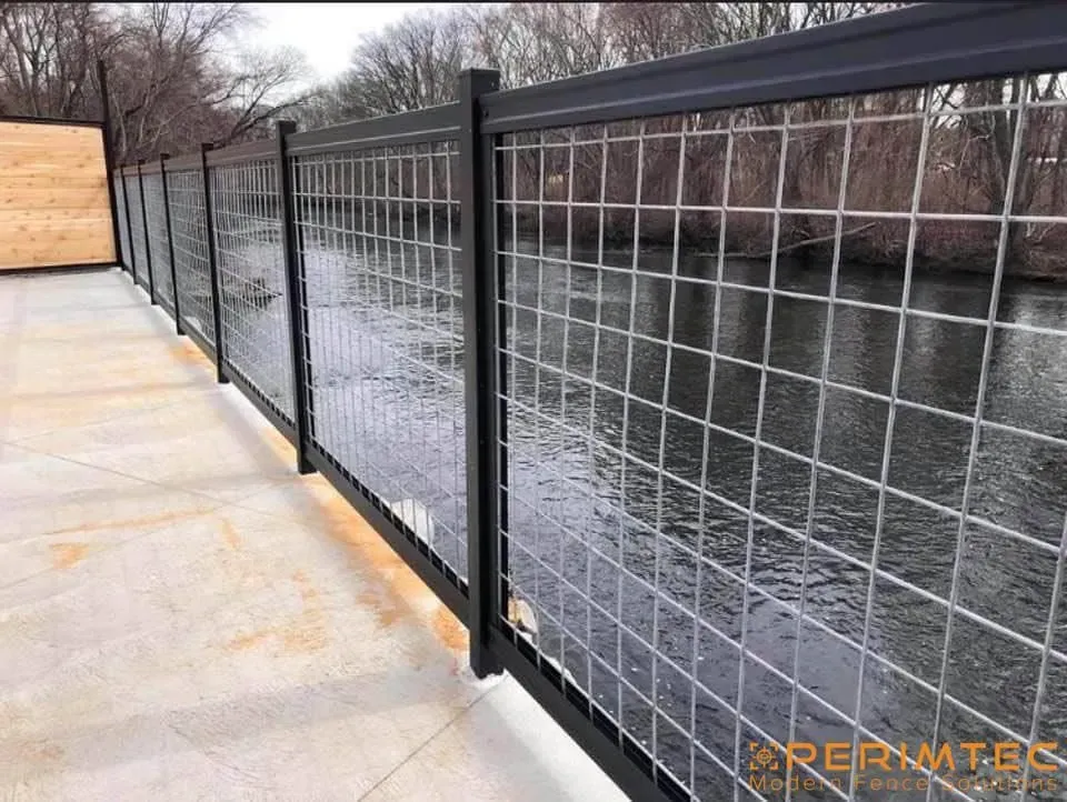 Black metal fence with wire mesh panels along a waterway.