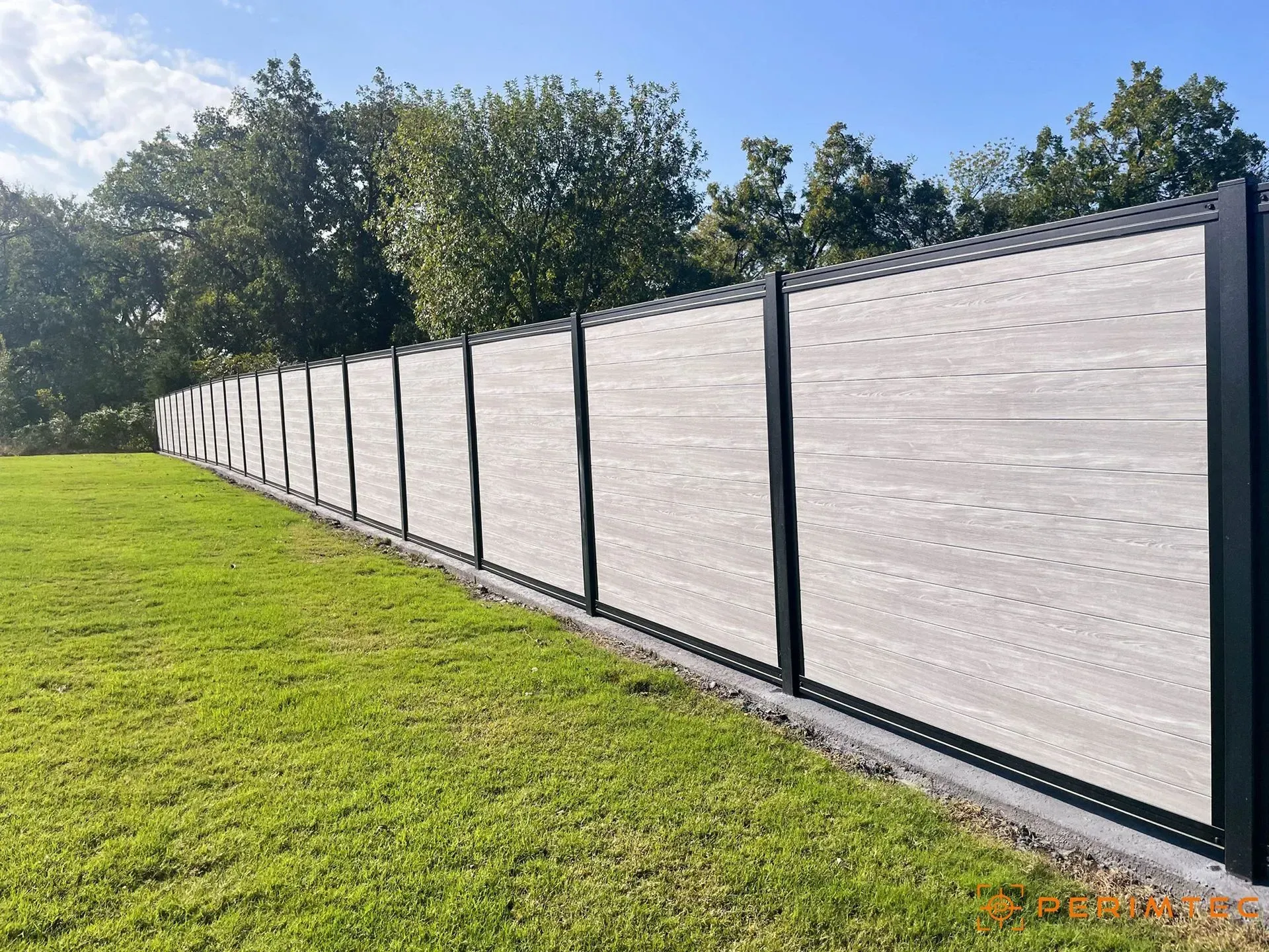 Gray and black modern fence in a grassy field against a blue sky.