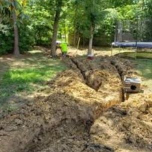 A trench dug in a backyard leading to a small box, with a person in the background.
