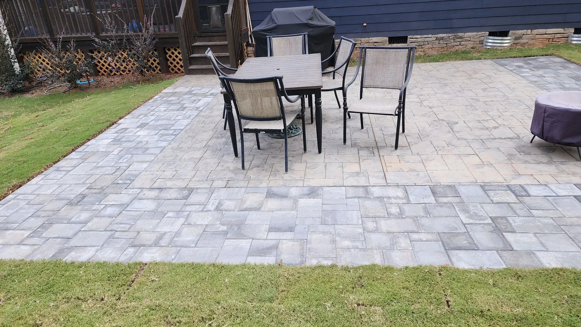 Patio with gray and tan pavers, outdoor dining set, fire pit, and surrounding grass.