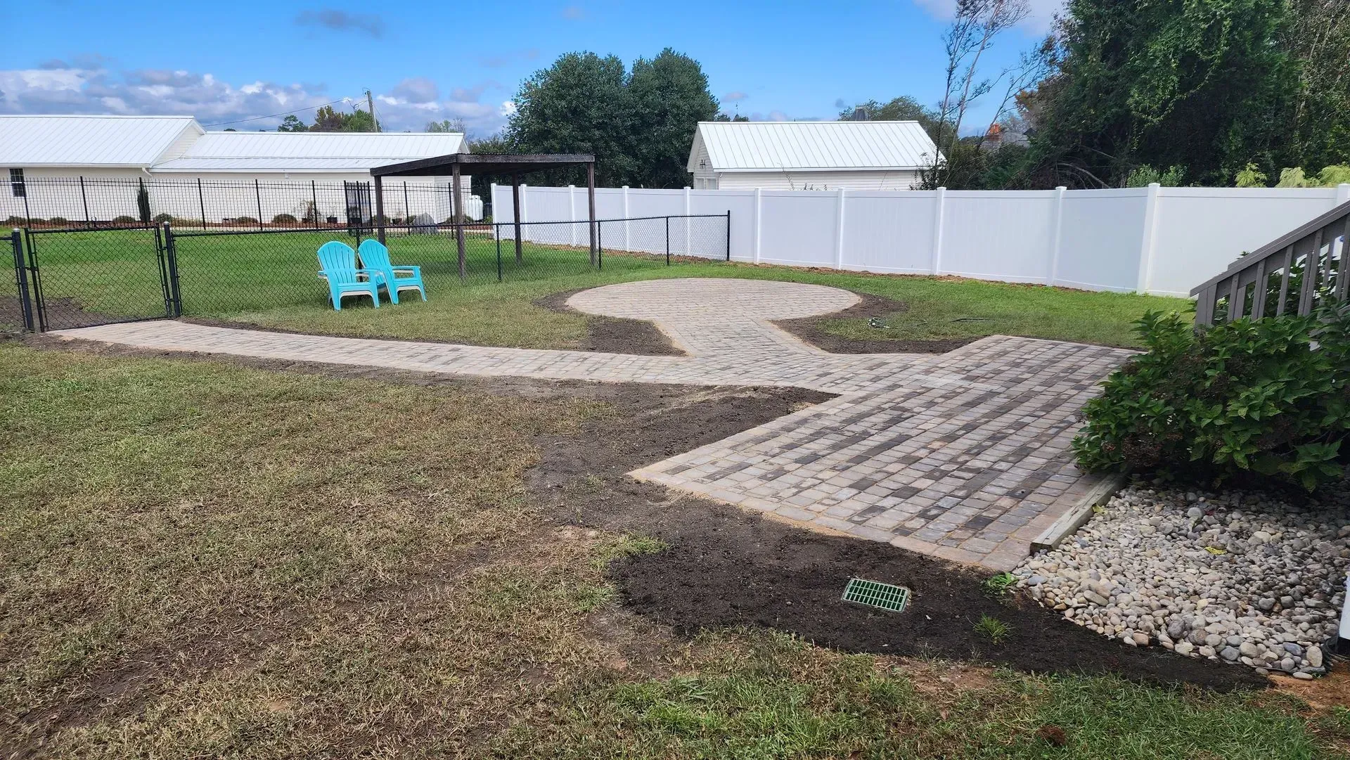 Backyard with a gravel path, a swing set, and a white fence under a blue sky.